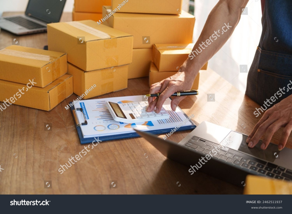 Warehouse staff calculating stock availability with a calculator and laptop. Omnichannel fulfillment streamlines inventory management and tally across multiple sales channels.